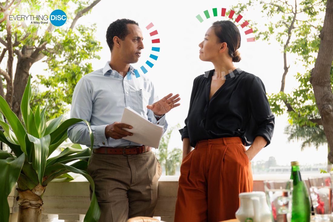 Two colleagues in conversation with the Everything DiSC halo graphic showing their individual DiSC styles